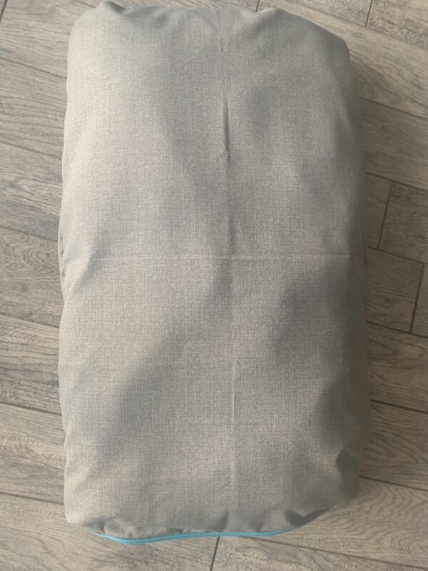 A grey colored dog bed bag on the floor