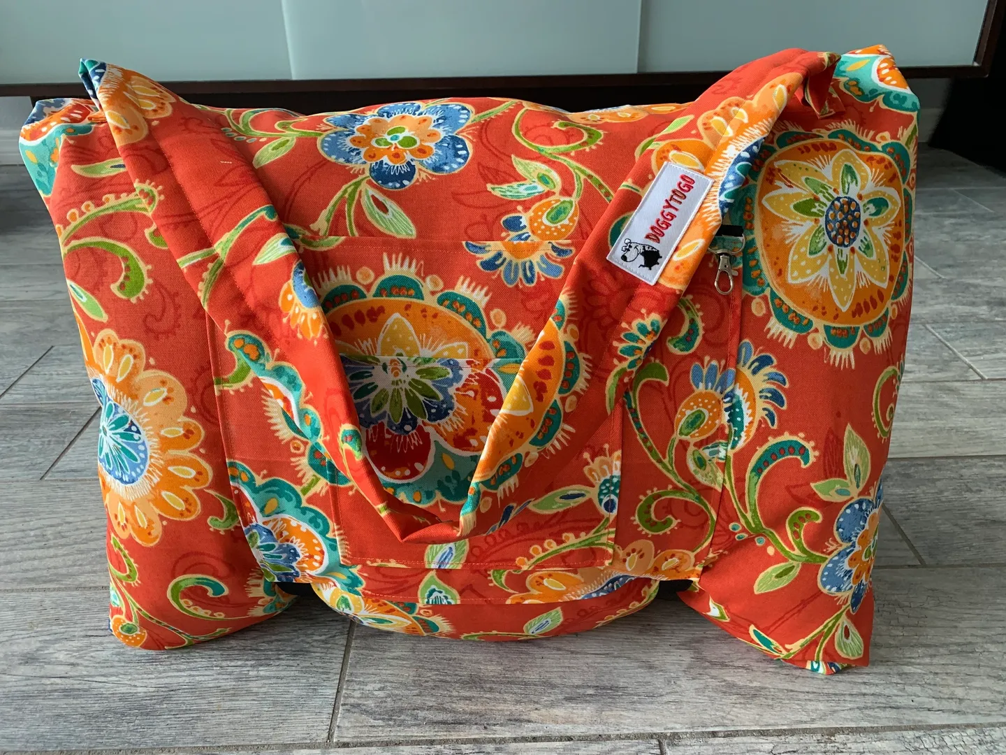 An orange color dog bed bag with flower designs printed on it