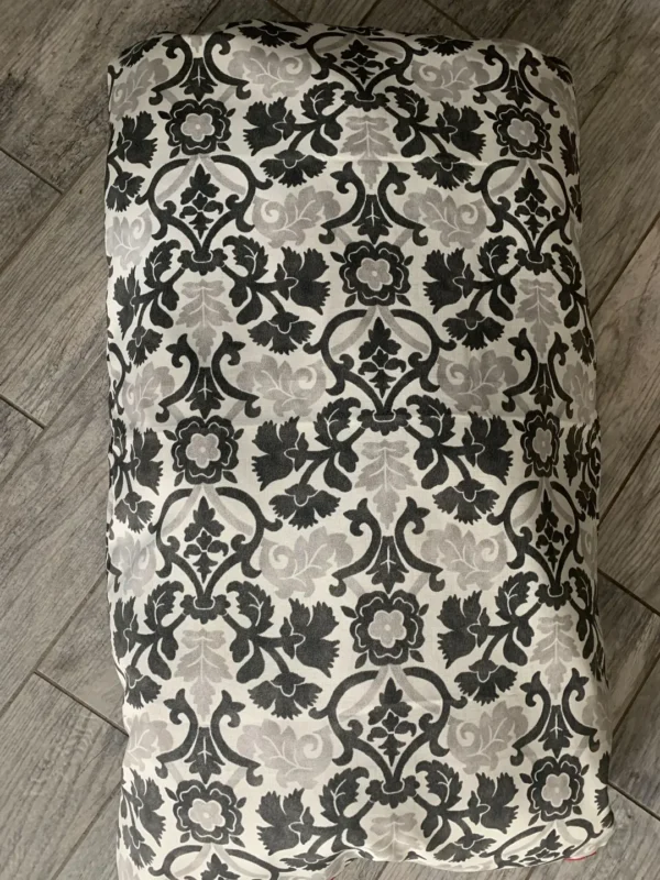 A small photograph of a white colored dog bed bag with grey and white designs kept on the floor