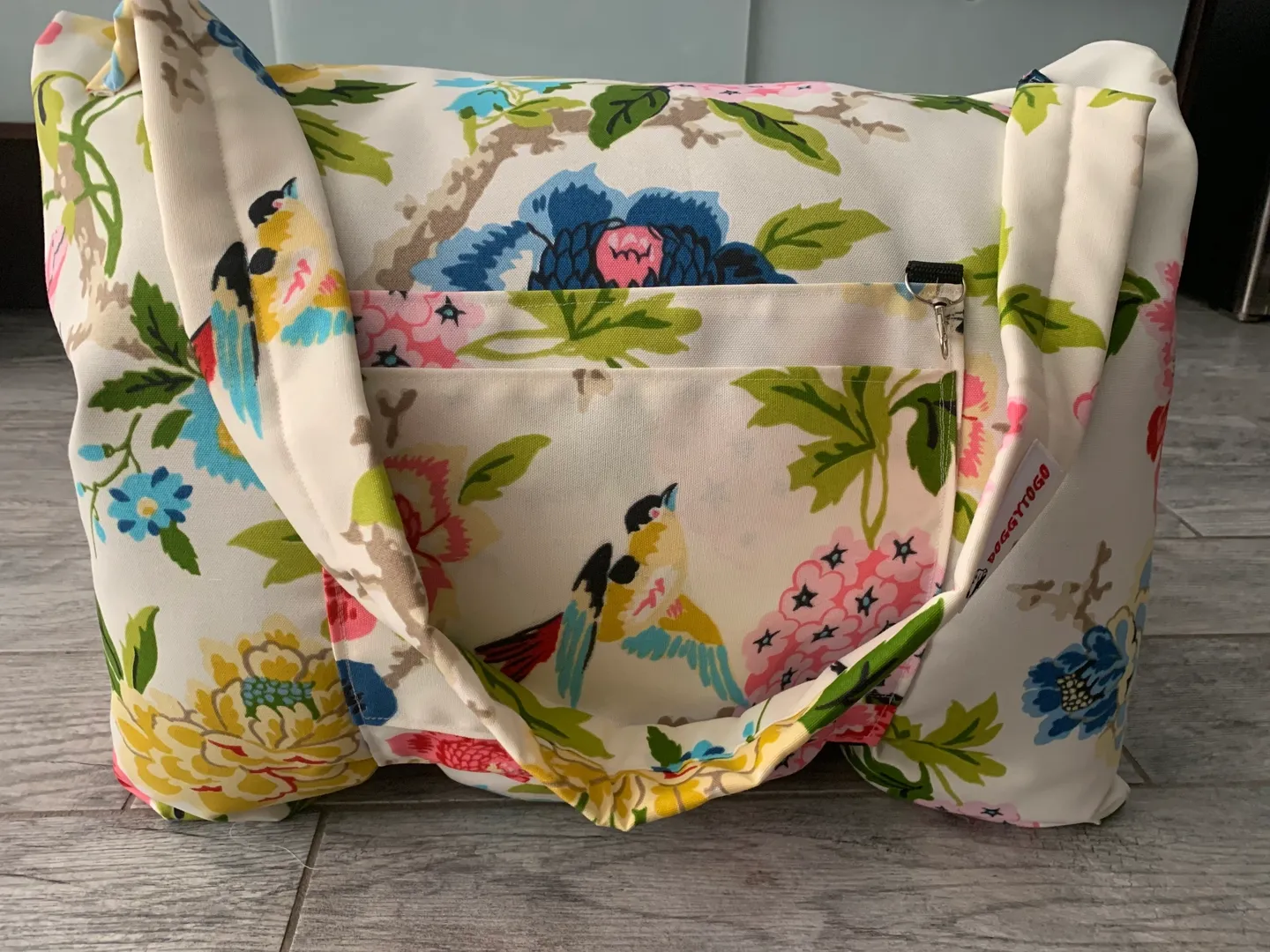 A white color dog bed bag with designs of birds, flowers, and leaves